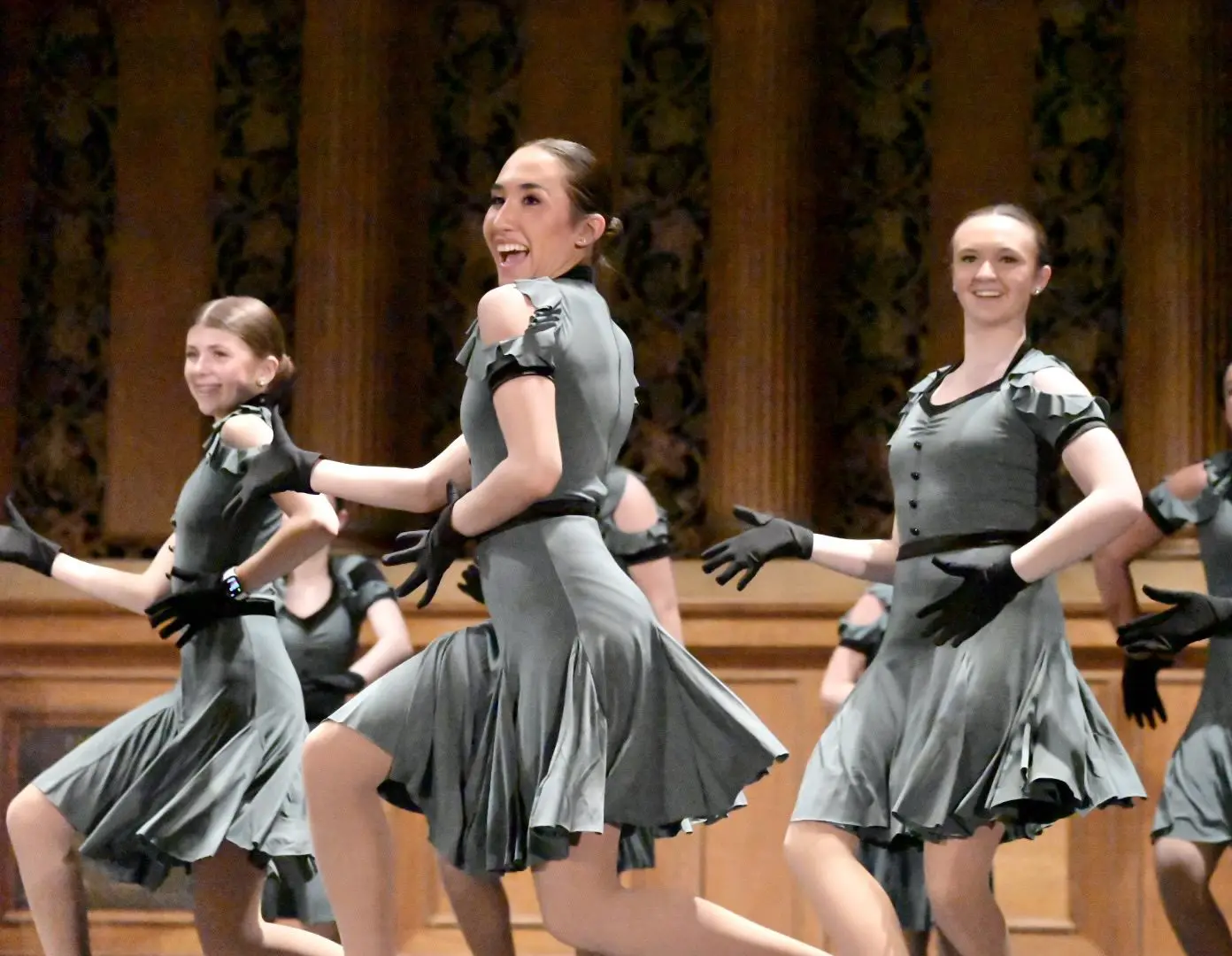 Three women in grey dresses are performing a dance.