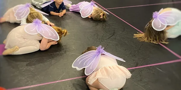 A group of children wearing fairy wings and laying on the ground.