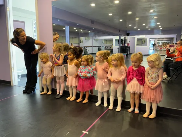 A group of little girls lined up in front of a man.