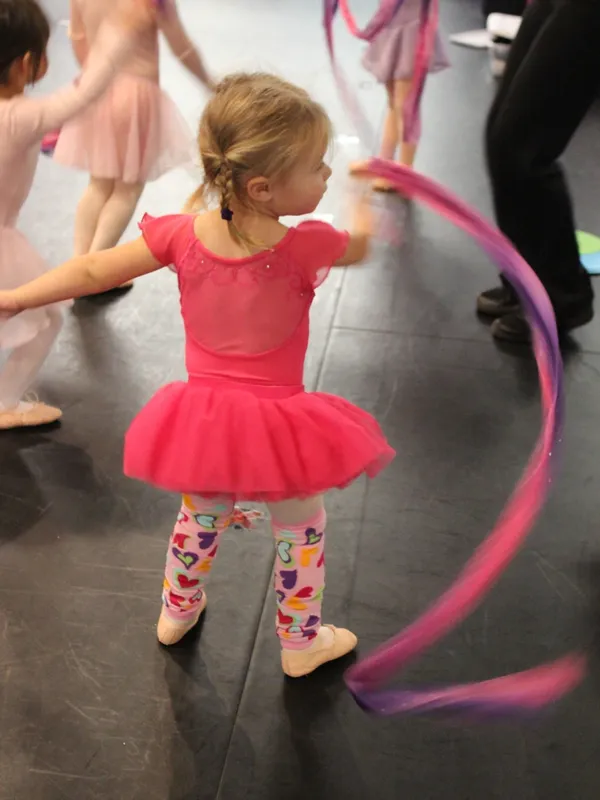 A little girl in pink dress holding onto a ribbon