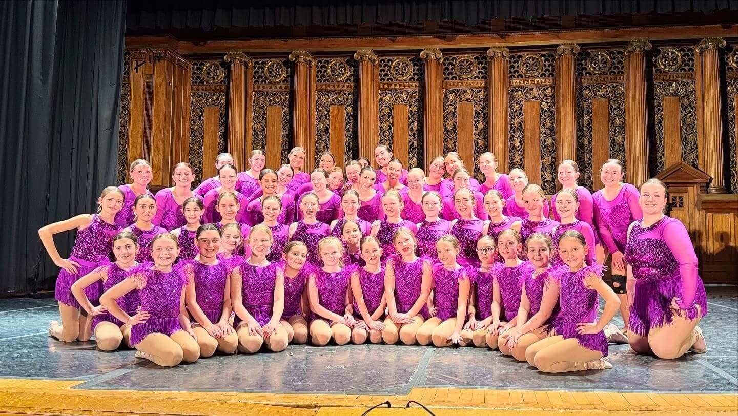 Smiling dancers posing in magenta fringe costumes